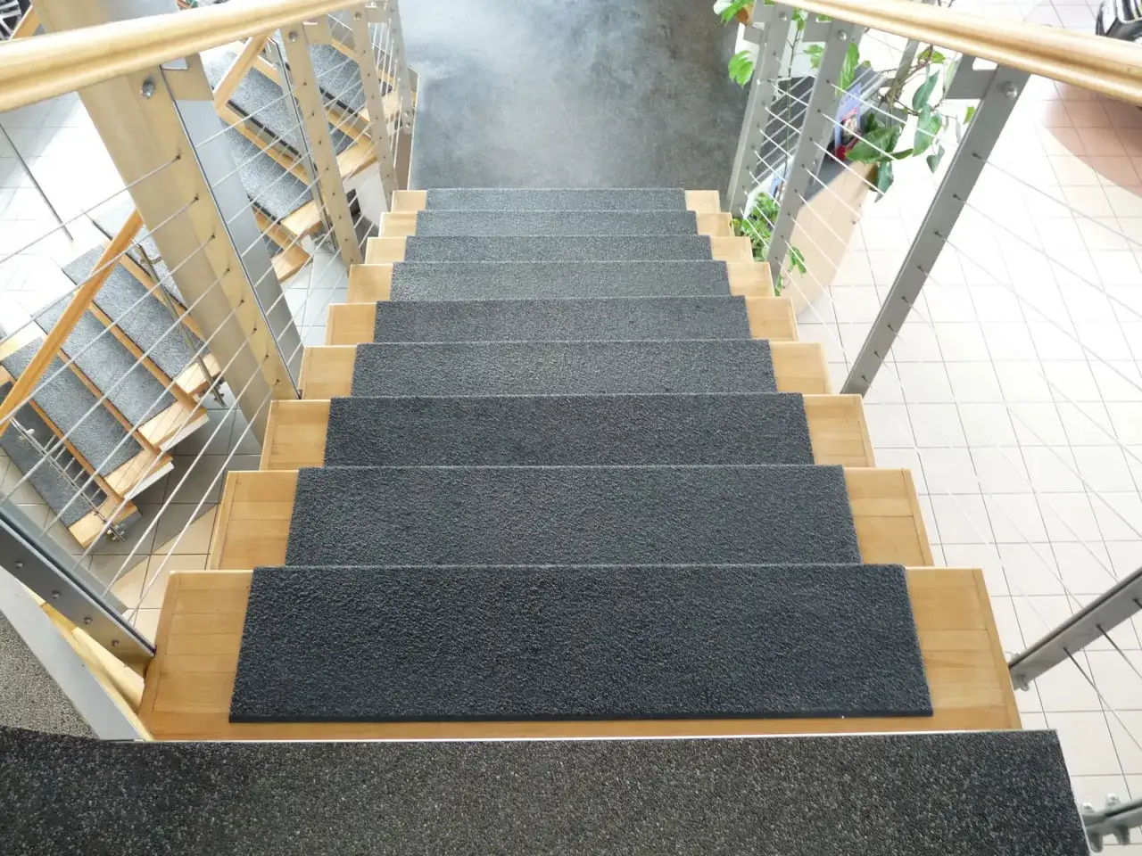 Schody z płytek w domu, z drewnianymi stopniami i metalową balustradą.