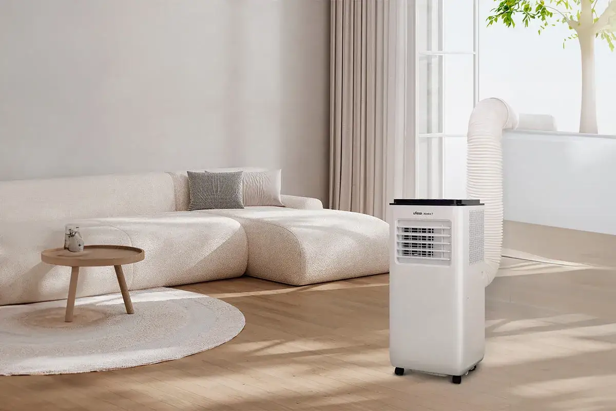 Un aire acondicionado portátil con tubo de evacuación, ideal para la renovación de aire en un salón moderno con sofá curvo y mesa auxiliar.