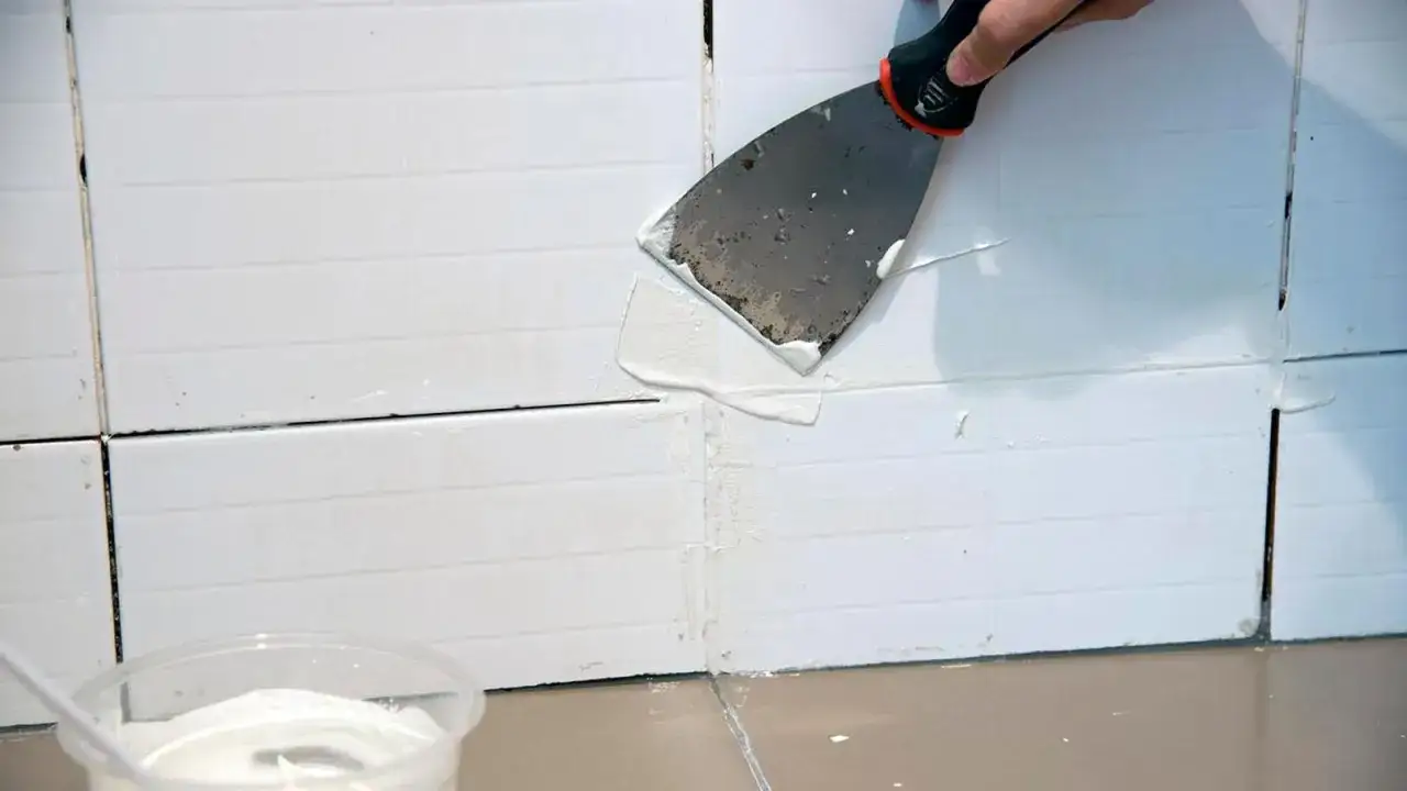 Aplicando masilla para limpiar juntas de azulejos blancos con una esp&aacute;tula.