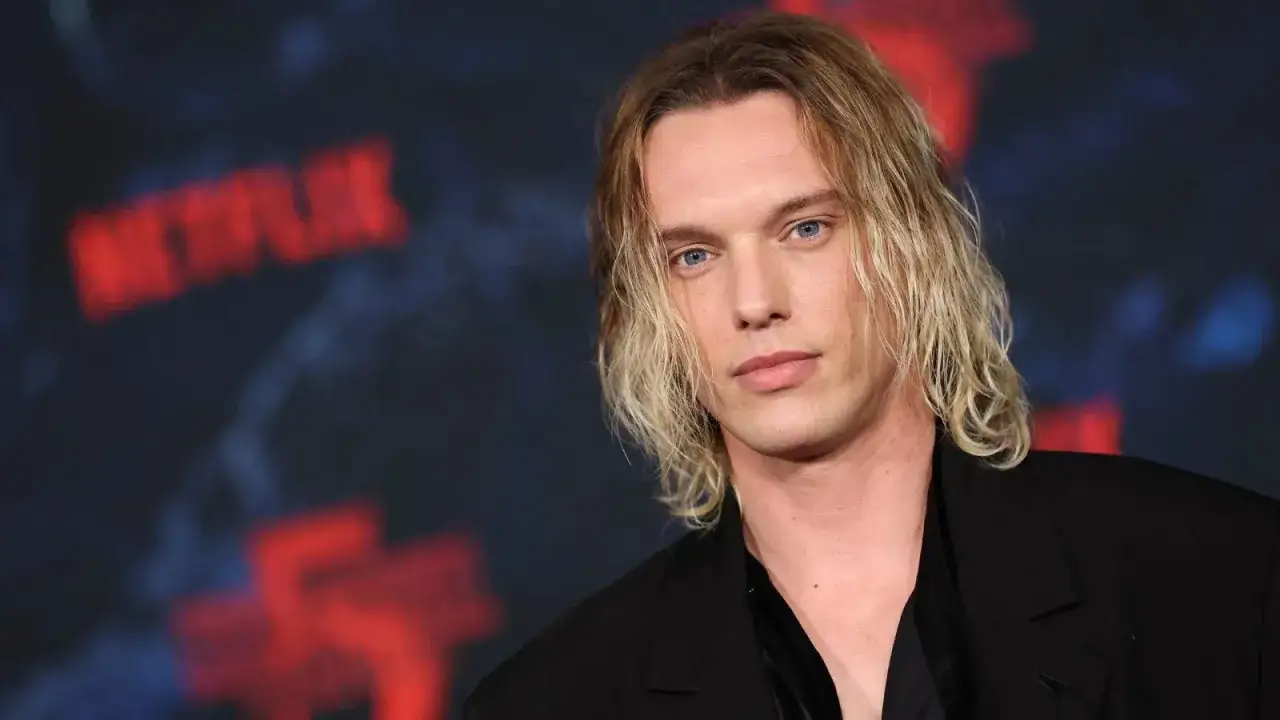 Jamie Campbell Bower, aktor wcielający się w Vecnę, z blond włosami i niebieskimi oczami, na tle logo Netflix.