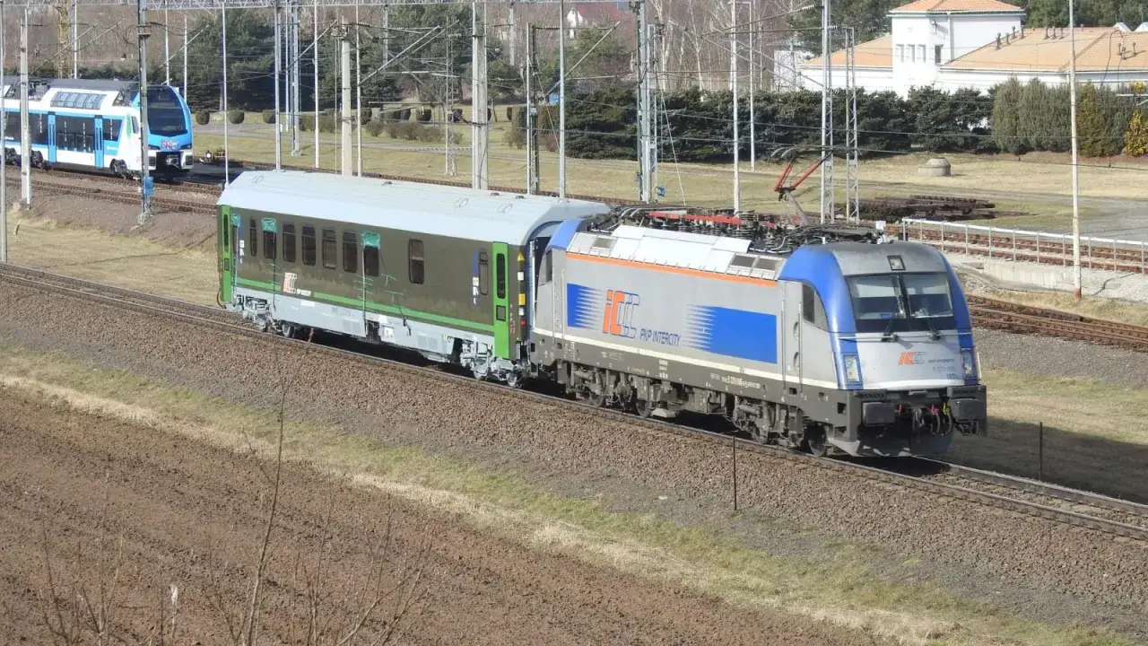 Pociąg PKP Intercity z zieloną górą wagonów mija krajobraz.