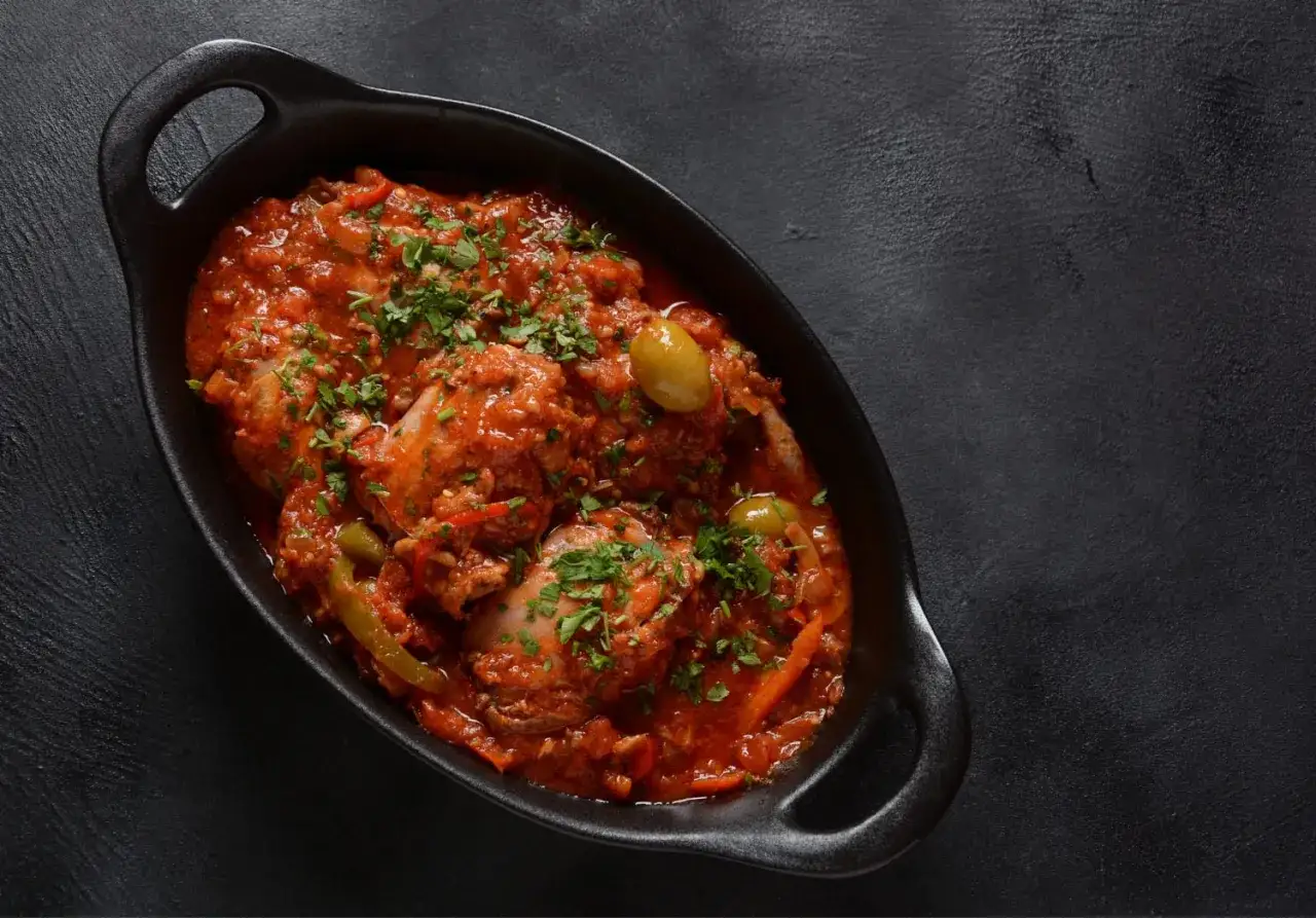 Pollo alla cacciatora ricetta della nonna, un piatto succulento con pomodoro, olive e prezzemolo, servito in una cocotte nera.