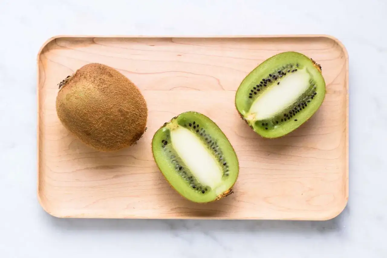 Un kiwi entier et deux moitiés sur un plateau en bois. Attention, ce kiwi langue qui pique peut surprendre !
