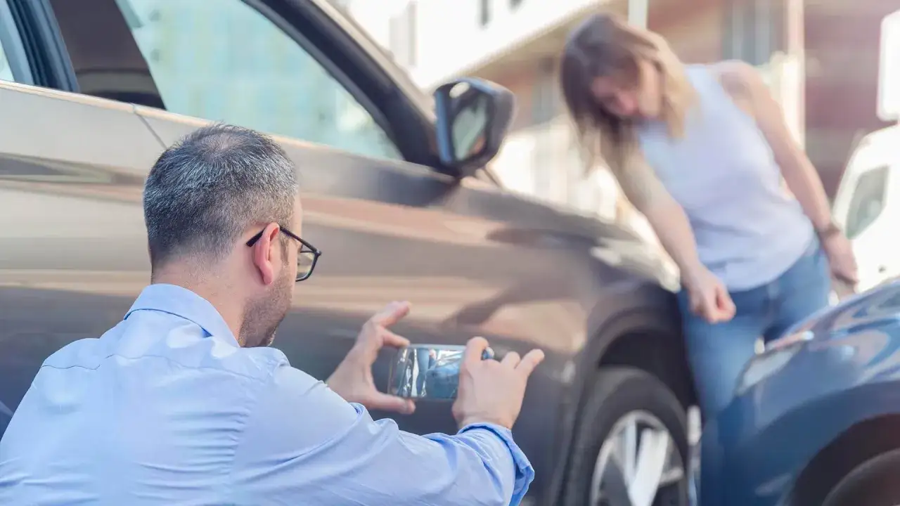 Man fotograferar parkeringsskada. Kvinnan verkar orolig, kanske en parkeringsskada smitning?