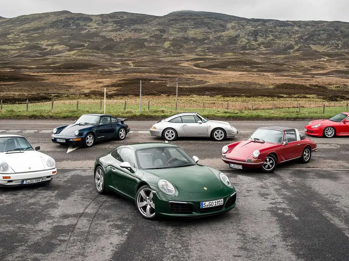 Kolekcja Porsche 911, w tym zielony model z tablicą S.GO 1911, zaparkowana na tle górskiego krajobrazu.