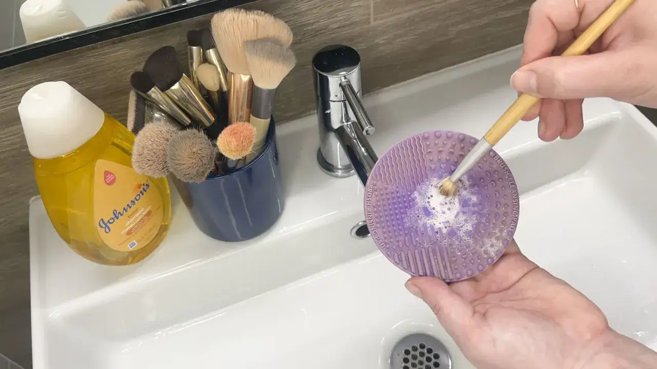 Demostración de como limpiar brochas de maquillaje con champú para bebés y una almohadilla limpiadora.