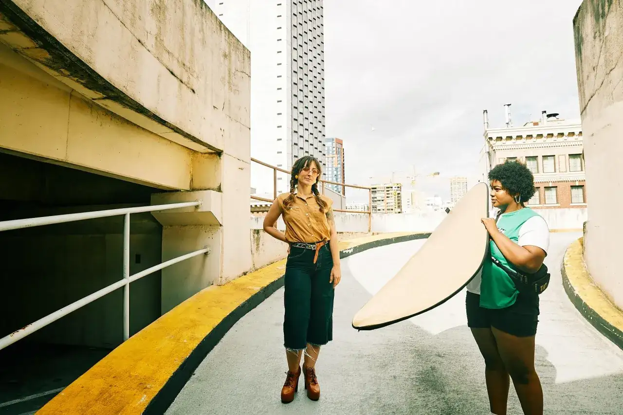 Due ragazze con una tavola da surf, in una **foto al sole** su un tetto con vista sulla città.