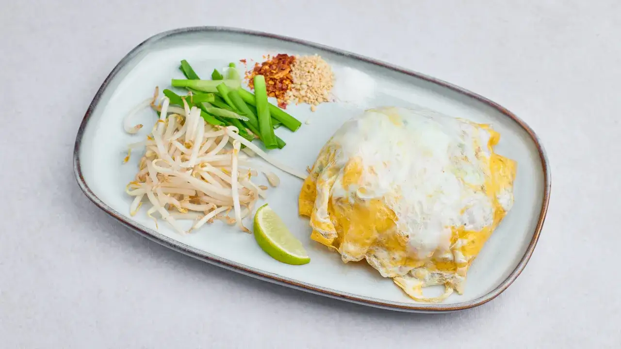 Oryginalny przepis na pad thai: danie z makaronem ryżowym, jajkiem, kiełkami, szczypiorkiem, chili i orzeszkami ziemnymi, podane z limonką.