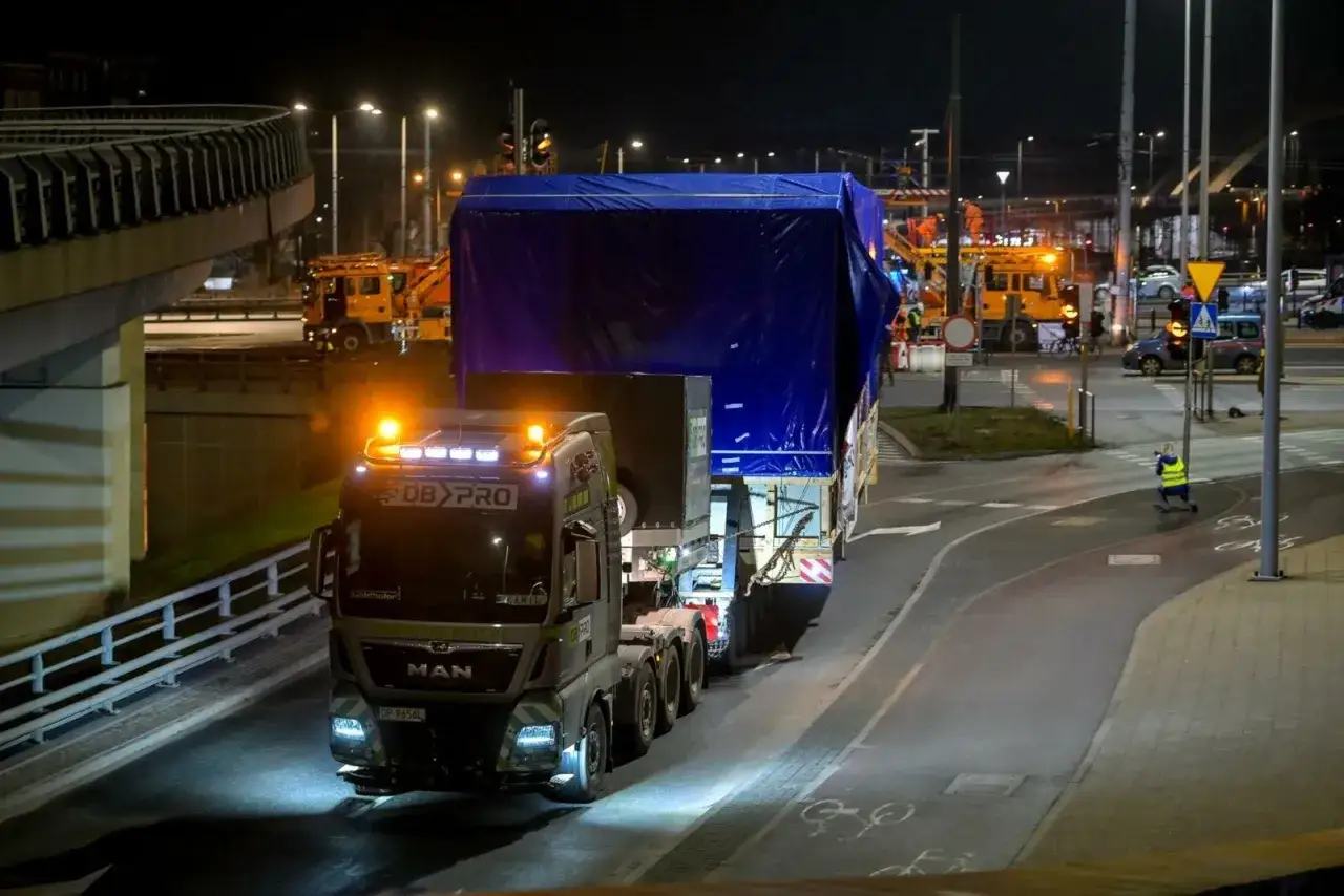 Ciężarówka MAN z naczepą przewozi ogromny ładunek pod niebieską plandeką. To największy transport w Polsce, który nocą pokonuje drogę.