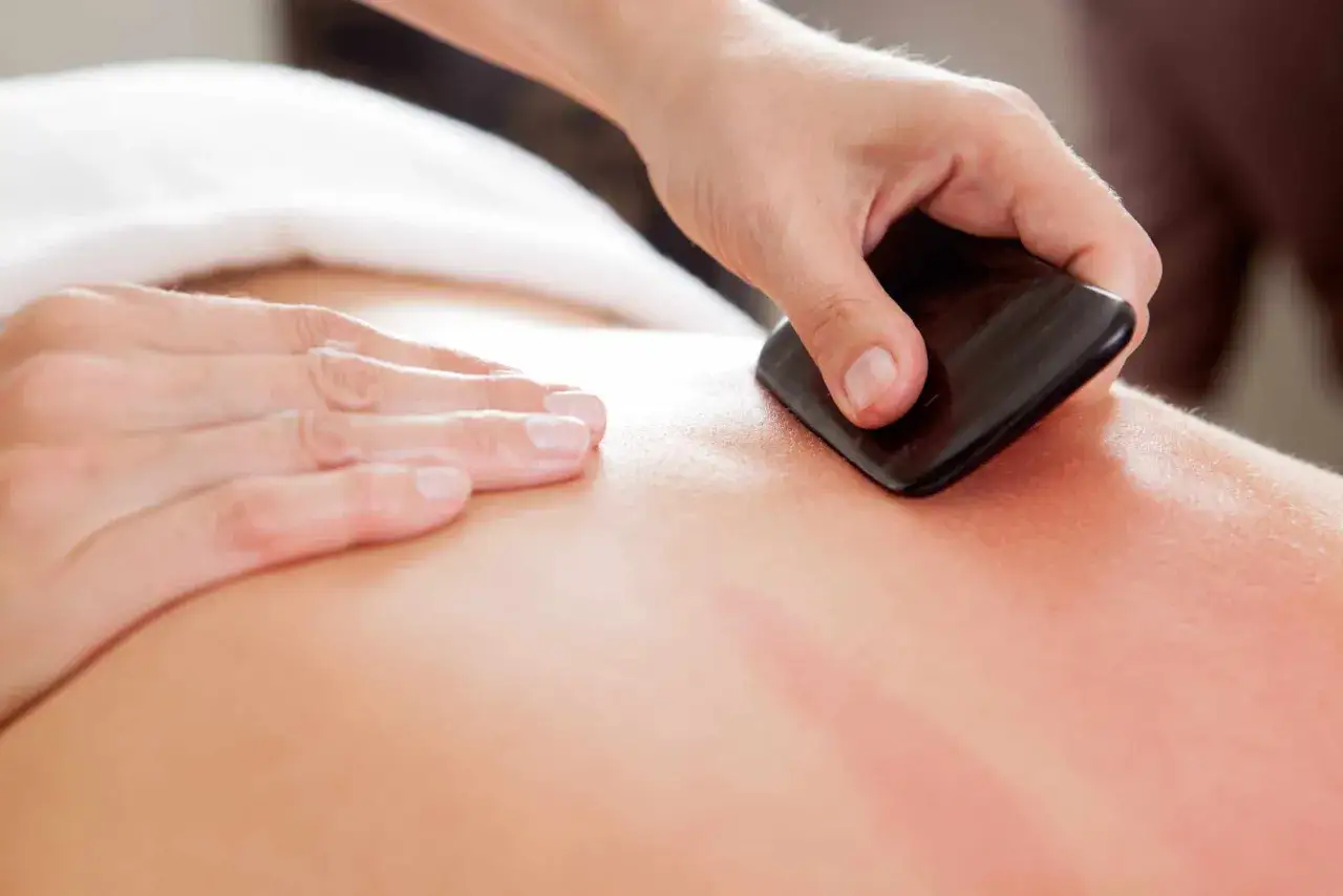 En hand utför en gua sha massage på en rygg, vilket skapar röda märken.