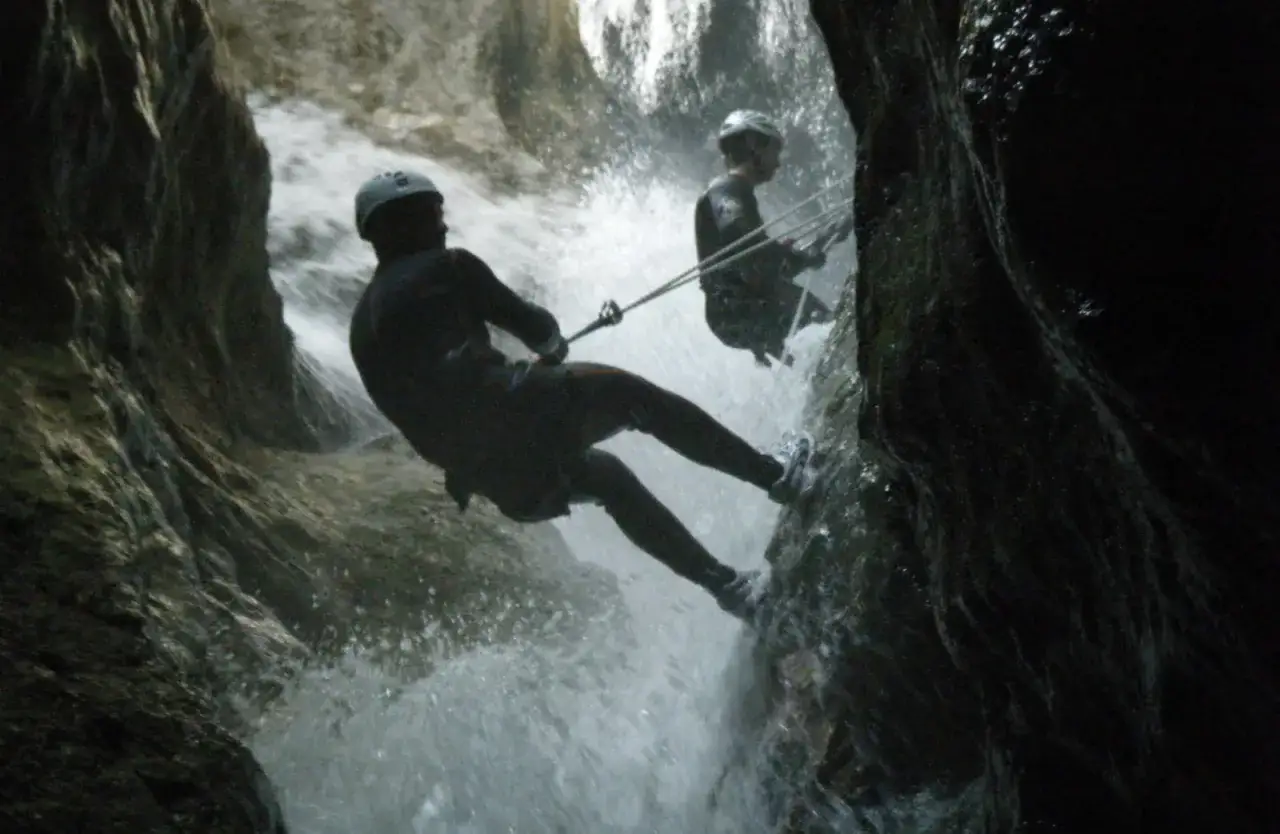 Due persone fanno **canyoning in Trentino**, calandosi con la corda lungo una cascata tra rocce scure.