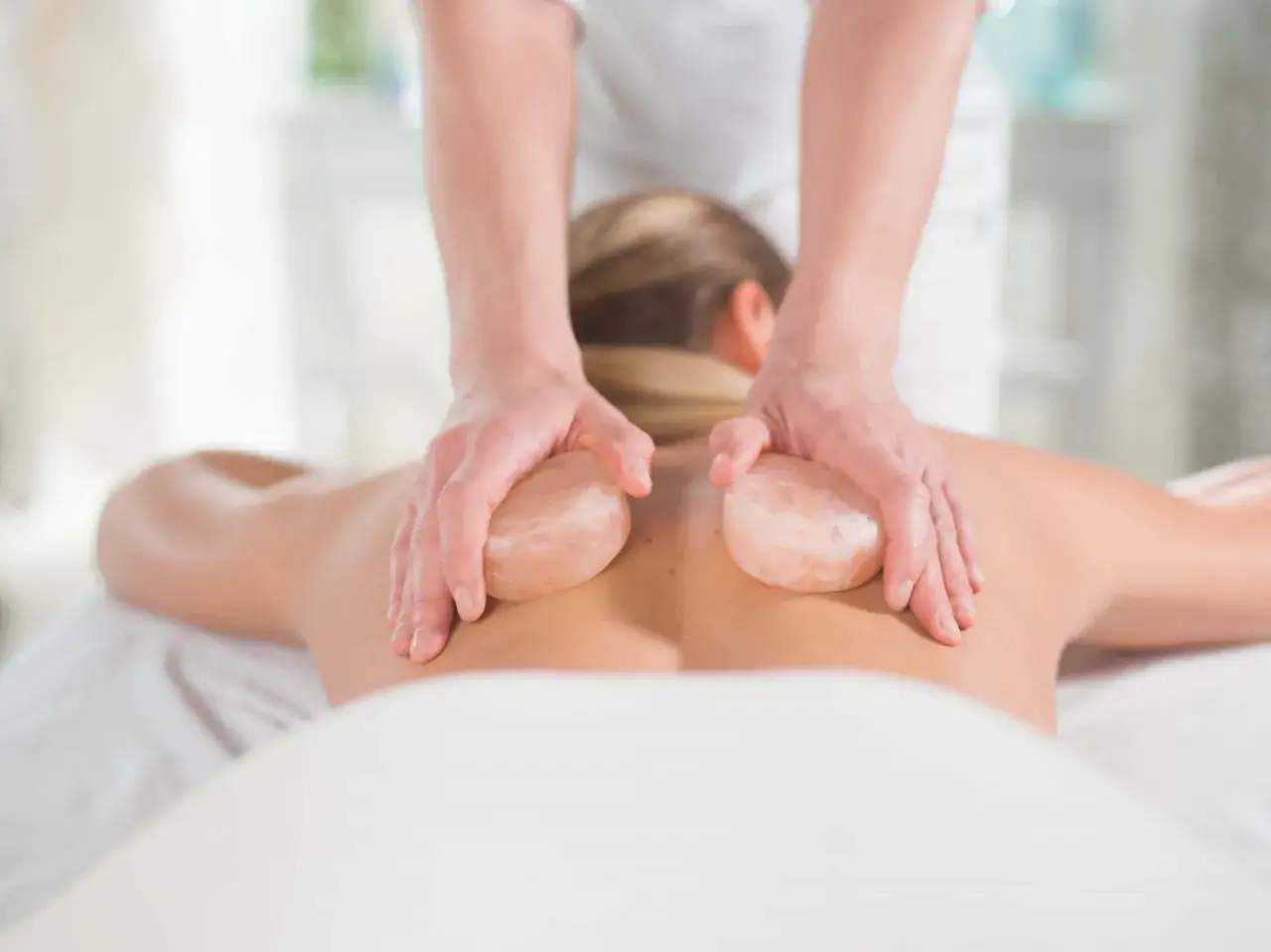 Hands performing a relaxing himalayan salt massage on a person's back, using warm salt stones.