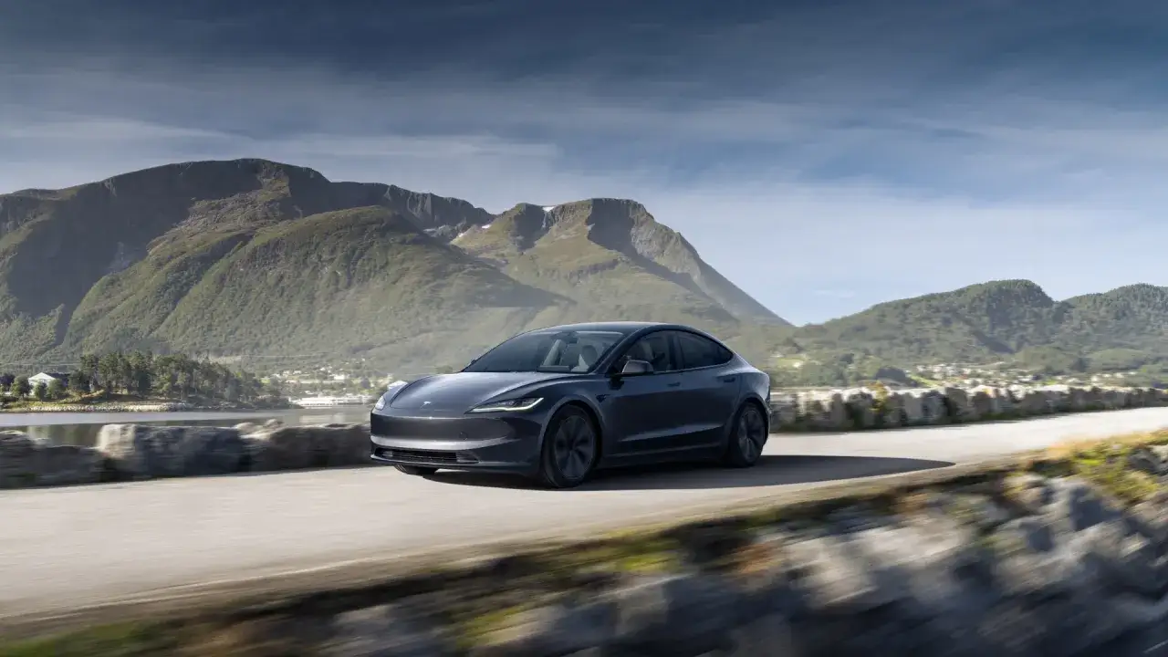 Szara Tesla mknie po drodze z widokiem na góry i jezioro. Czy Tesla jest tylko elektryczna? Ta podróż pokazuje, że tak.