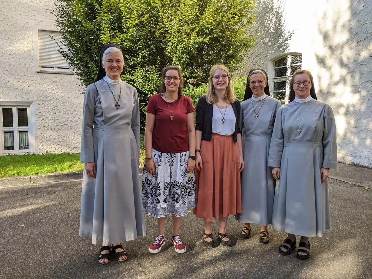 Fünf Frauen, drei davon Nonnen, stehen vor einem Gebäude. Vielleicht planen sie, ins Kloster zu gehen.