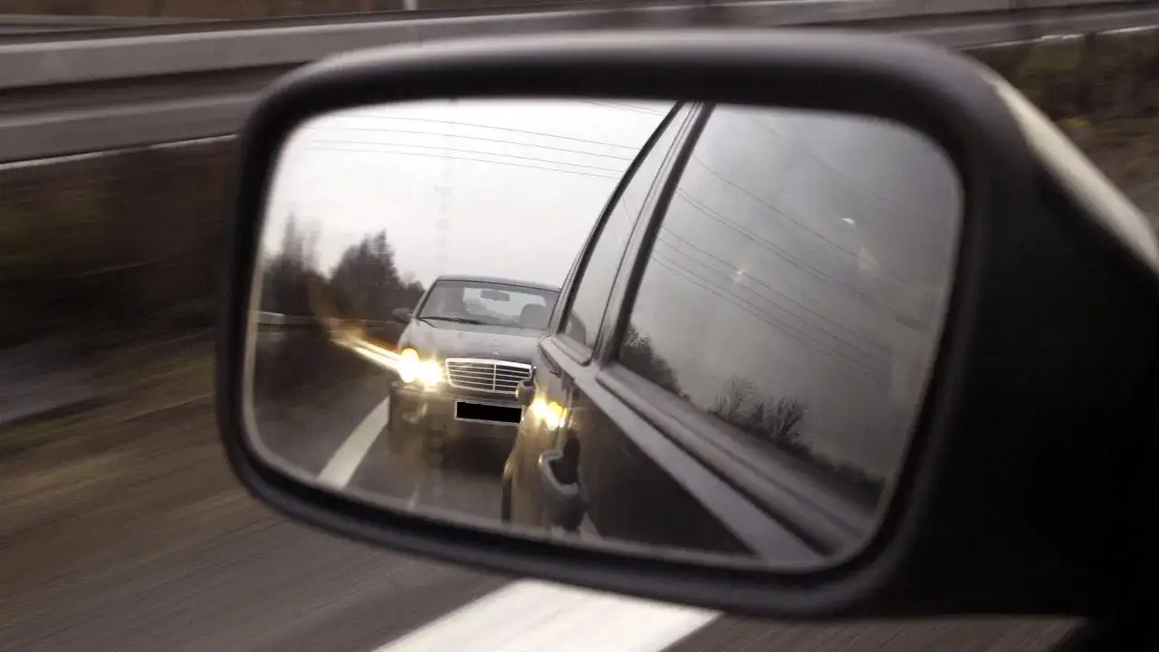 Ein Auto drängelt auf der Autobahn und gibt Lichthupe. Der Fahrer im Rückspiegel wird geblendet.