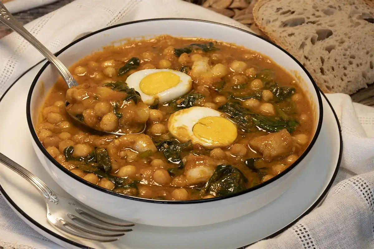 Un reconfortante potaje de vigilia con garbanzos, espinacas y huevo duro, servido en un cuenco blanco.