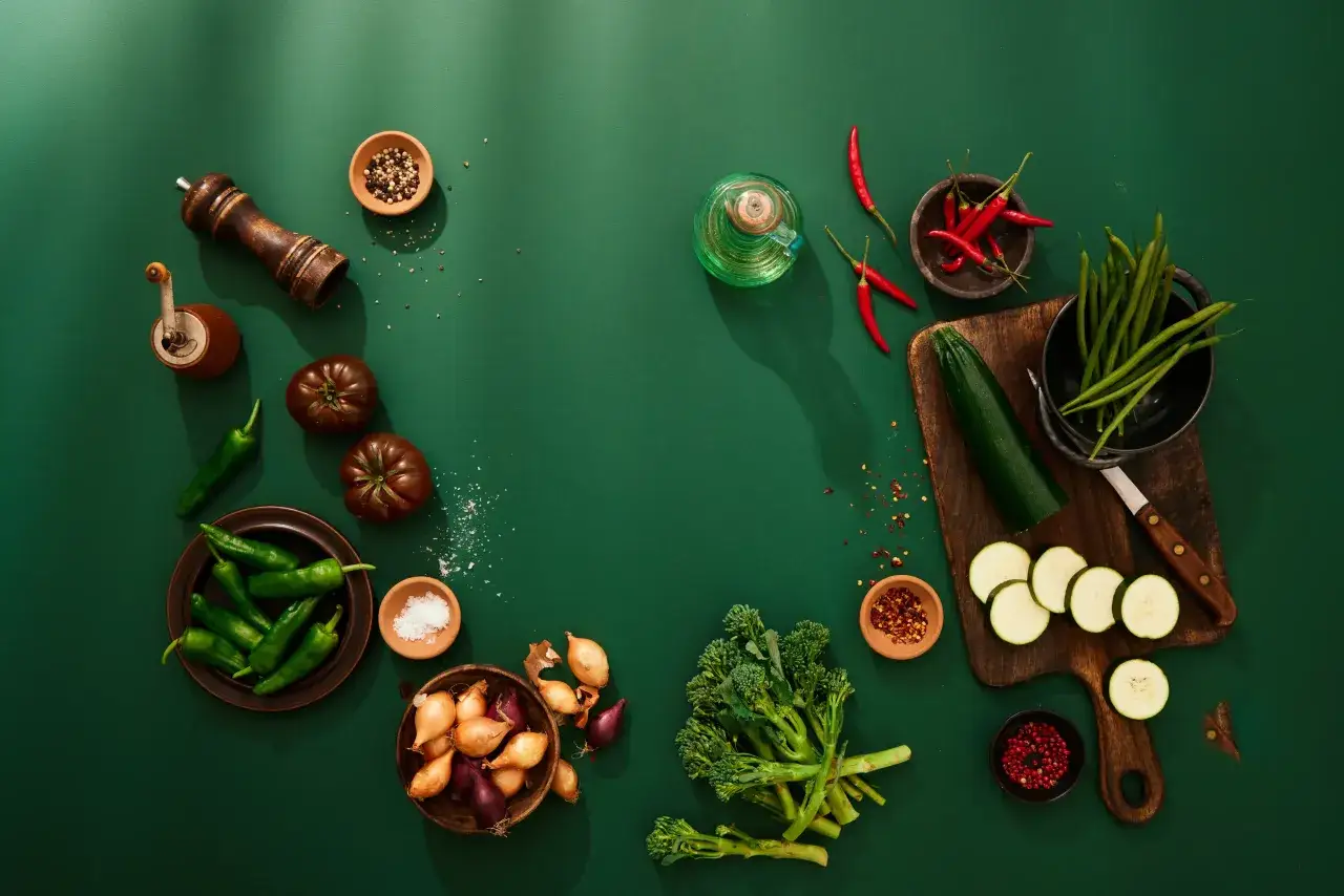 Grönsaker som chili, tomat, zucchini och broccoli ligger utspridda. En pepparkvarn och salt i skålar antyder att man funderar på hur man får bort salt smak.