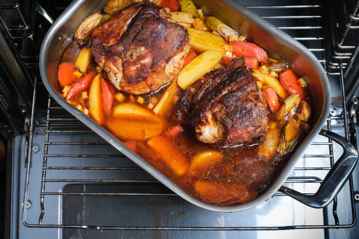Zwei saftige Stücke schweinebraten im schmortopf mit Kartoffeln und Wurzelgemüse garen im Ofen.