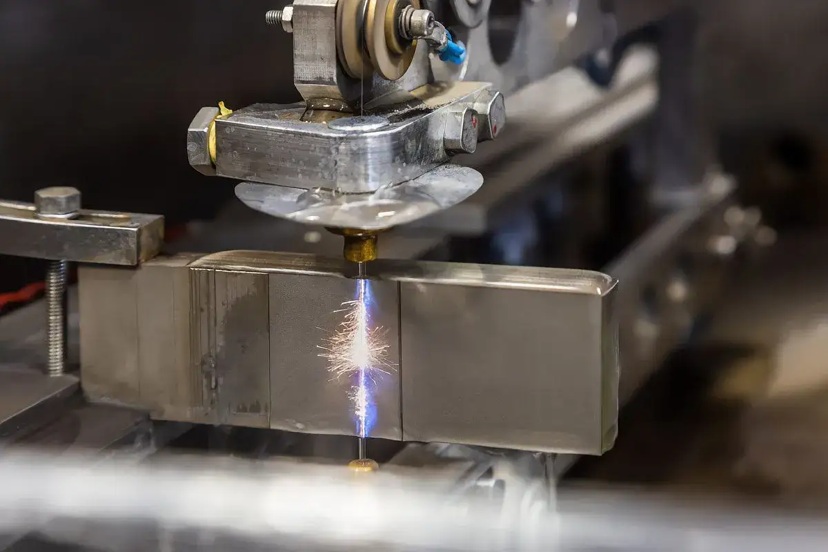 Precyzyjna obróbka elektroerozyjna metalowego bloku, iskry rozchodzą się od drutu tnącego.