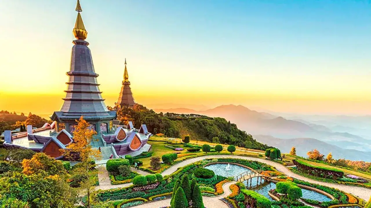 Dos templos dorados coronan una colina en Tailandia, con jardines exuberantes y montañas al amanecer. ¡Un lugar imperdible qué ver en Tailandia!