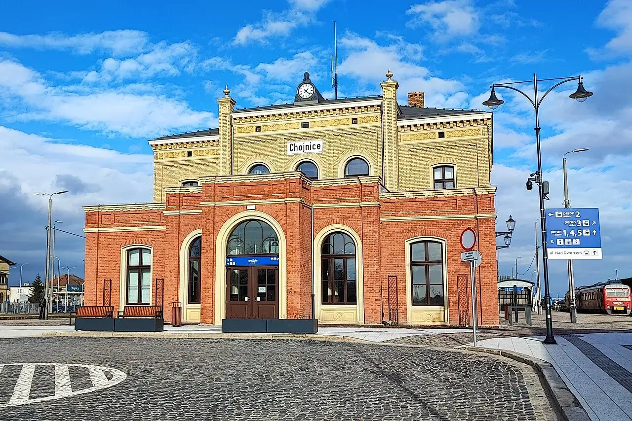 Dworzec kolejowy w Chojnicach, malowniczym mieście na trasie Piła-Chojnice, z charakterystyczną ceglaną fasadą i żółtą częścią górną.