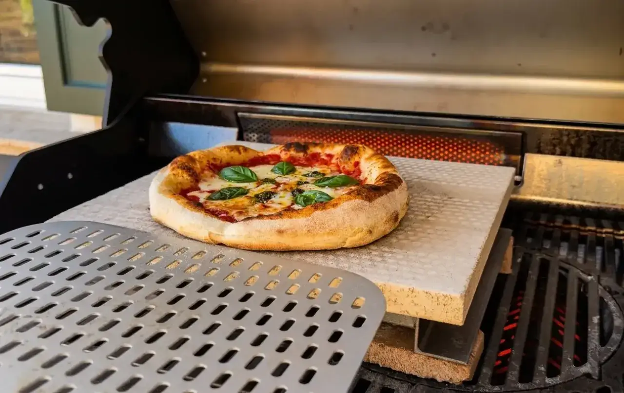 Leckere Pizza auf dem Gasgrill, goldbraun gebacken, mit frischem Basilikum und geschmolzenem K&auml;se.