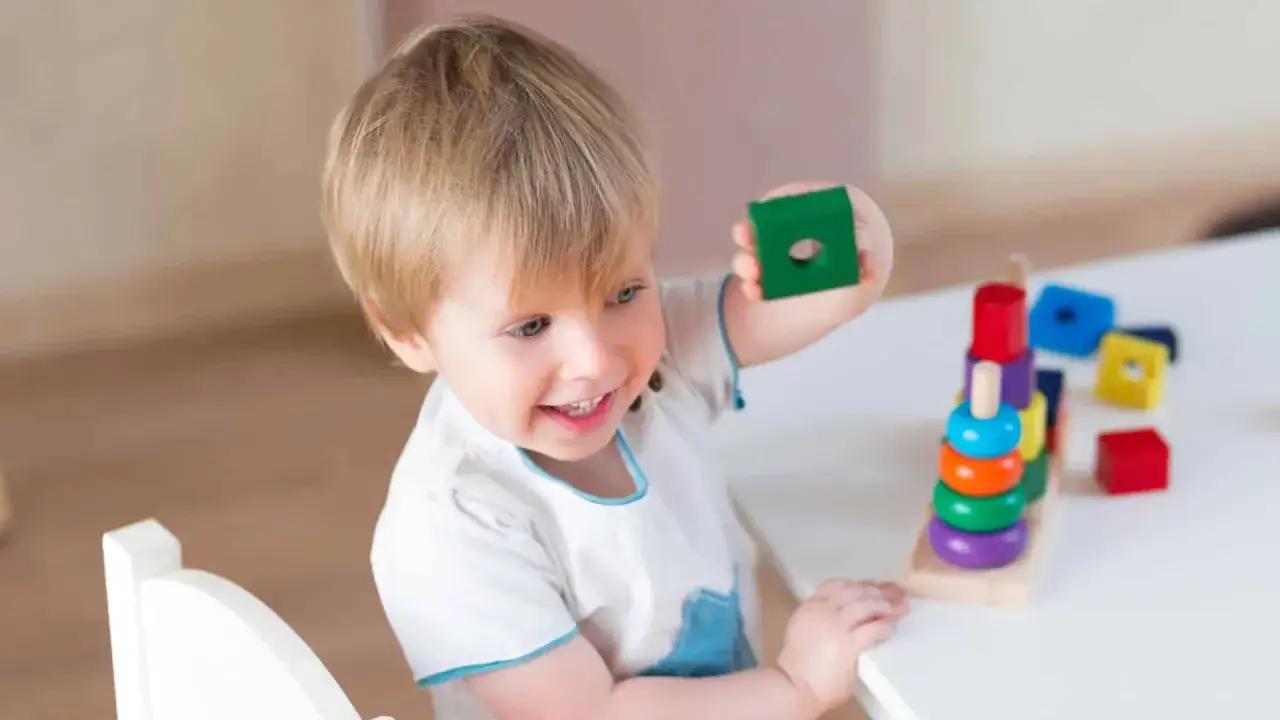 Bambino 3 anni sorridente gioca con blocchi colorati impilati.