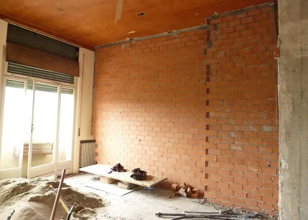 Interno in fase di ristrutturazione edilizia, con pareti in mattoni a vista, cumuli di sabbia e materiali da cantiere.