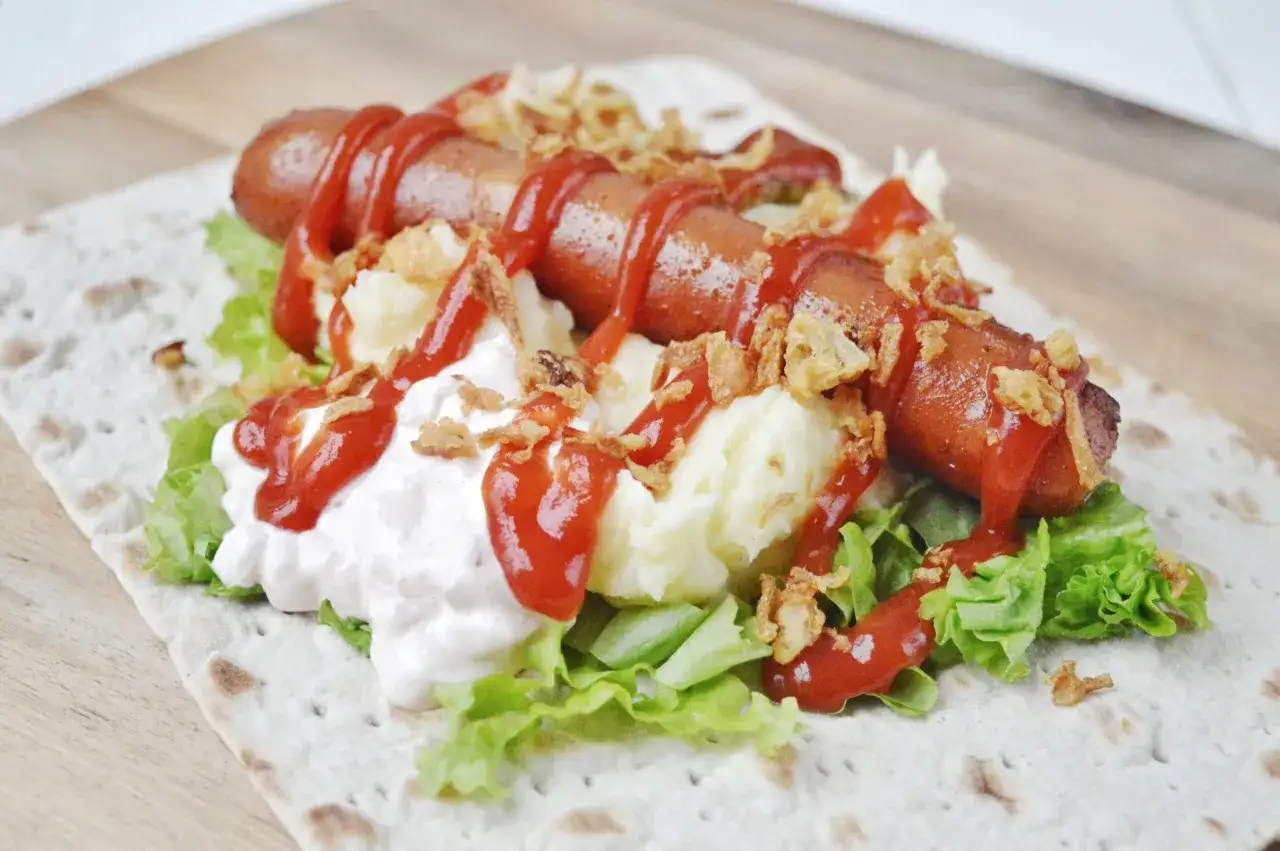 En svensk korv med mos, sallad, ketchup och friterad lök på ett tunnbröd. En riktig klassiker!