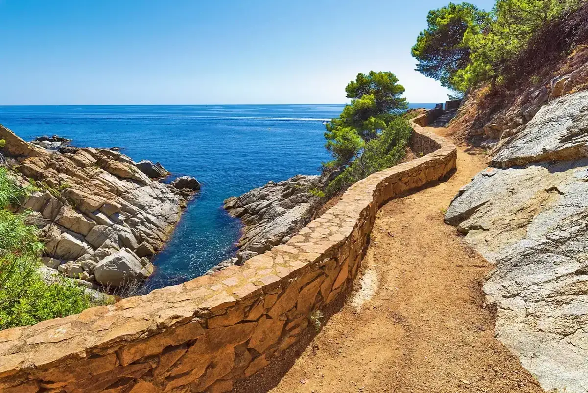 Ein malerischer K&uuml;stenpfad l&auml;dt zum Wandern in Spanien ein. Der Weg schl&auml;ngelt sich entlang der Felsen und des tiefblauen Meeres.