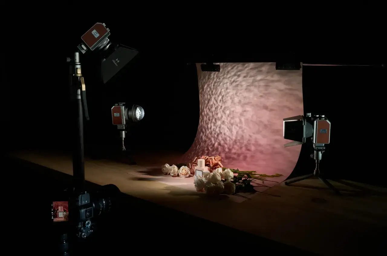 Profesjonalne ustawienie aparatu do fotografii produktowej: flakon perfum i róże na tle z efektem świetlnym.