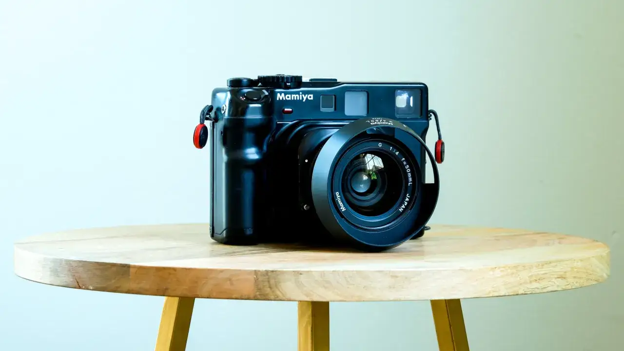A black Mamiya 645 camera with a 50mm lens sits on a wooden table, ready to capture timeless moments.