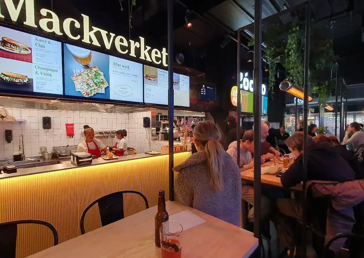 En livlig stockholm food court med folk som äter och personal som jobbar bakom disken.