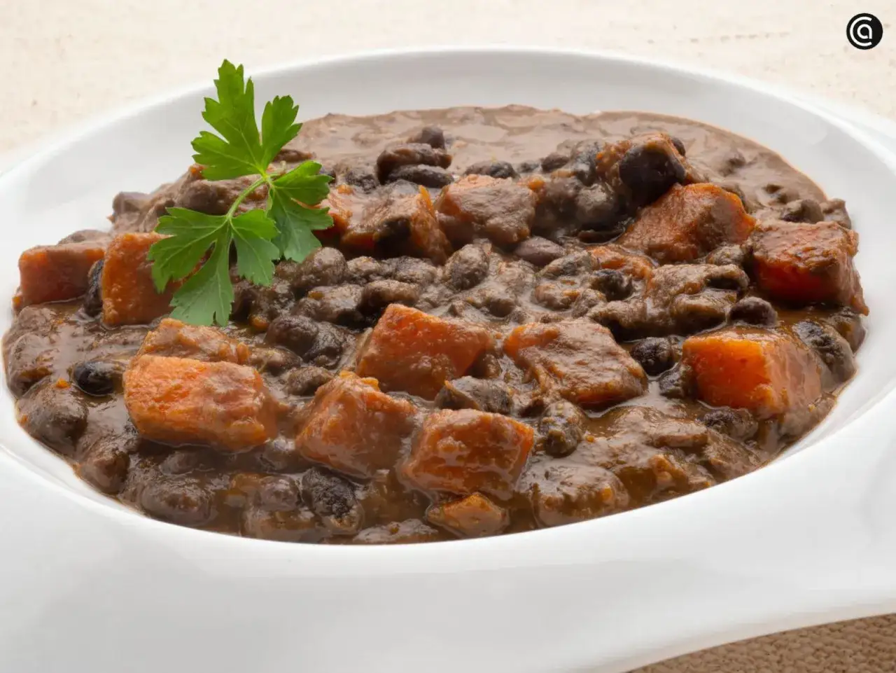 Un plato de frijoles negros con trozos de camote y perejil fresco.