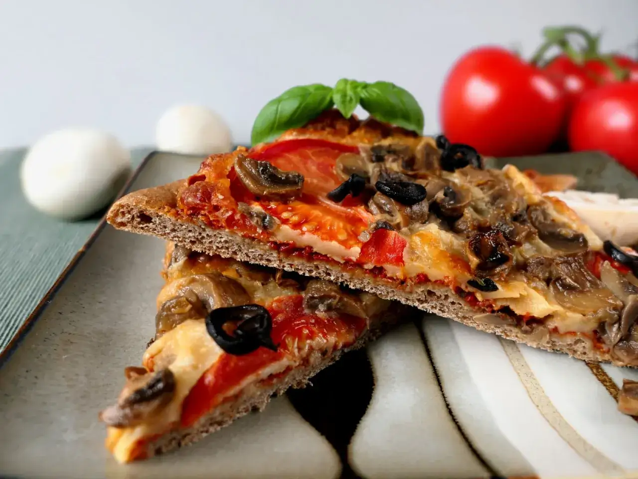 Dwie kromki pysznej pizzy dla cukrzyka z pieczarkami, oliwkami i pomidorami na pełnoziarnistym cieście.