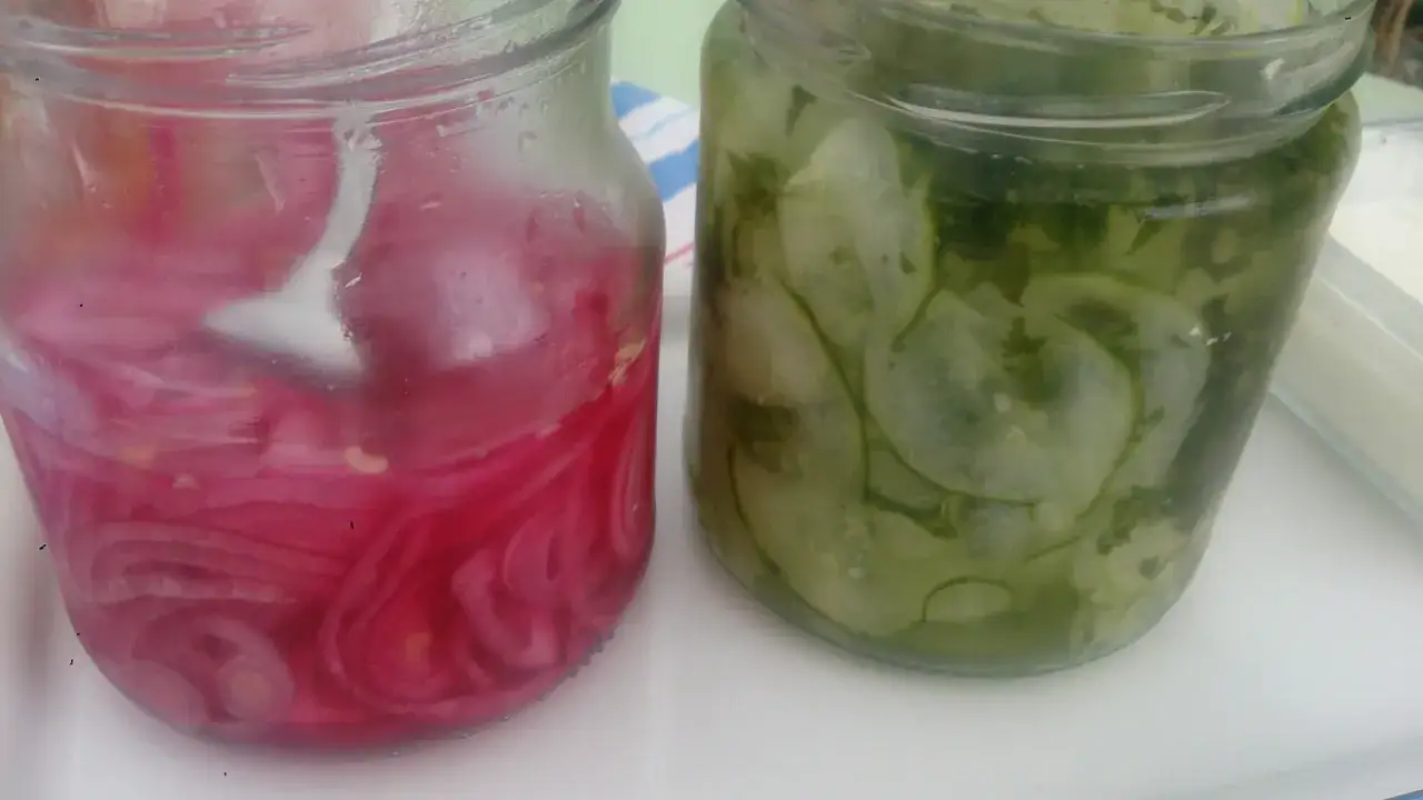 Tv&aring; glasburkar med inlagd gurka och r&ouml;dl&ouml;k. Den ena burken inneh&aring;ller skivad gurka med dill, den andra tunt skivad r&ouml;dl&ouml;k i en rosa lag.