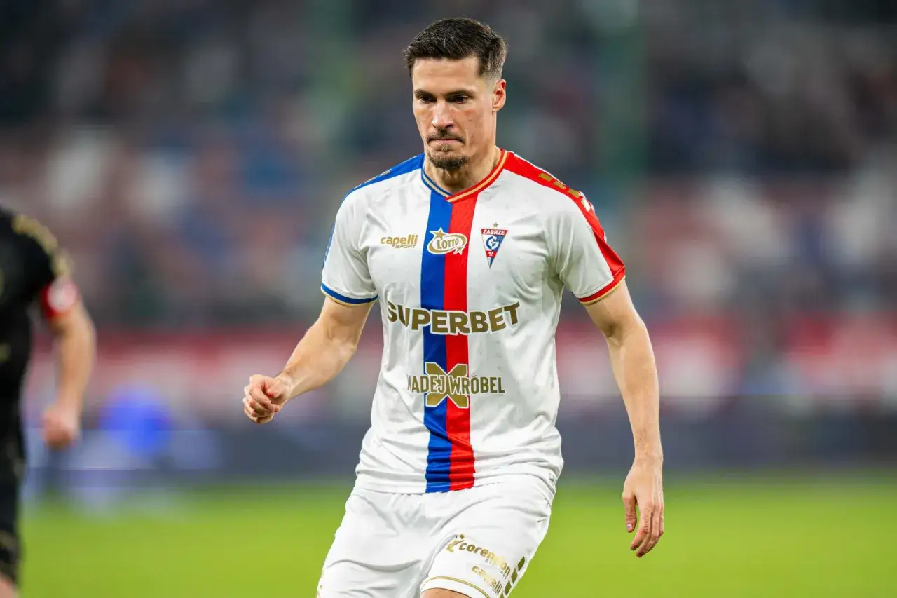 Piłkarz Górnika Zabrze w białej koszulce z czerwono-niebieskim pasem, gotowy do gry przeciwko Rakowowi Częstochowa.