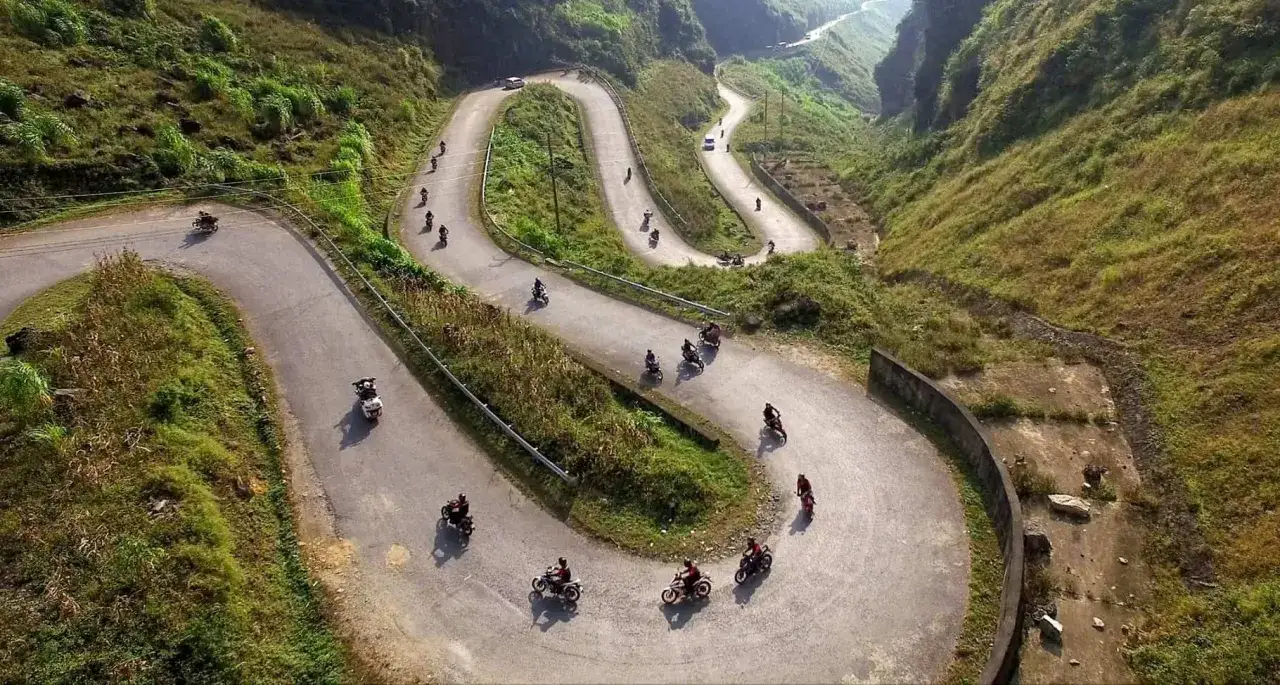 Motocykliści pokonują serpentyny na malowniczej trasie Ha Giang Loop, otoczeni zielonymi wzgórzami.