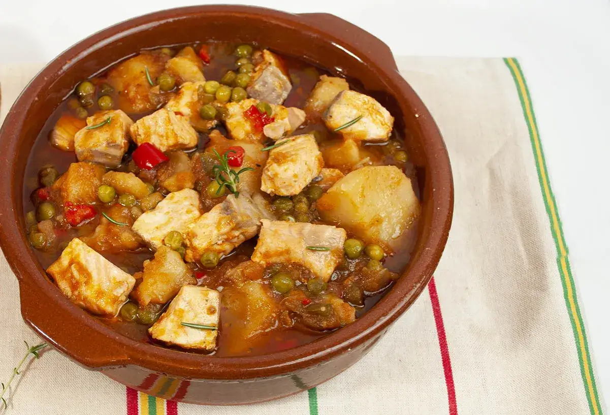 Un delicioso marmitako de salmón con patatas, guisantes y pimientos rojos, servido en cazuela de barro.