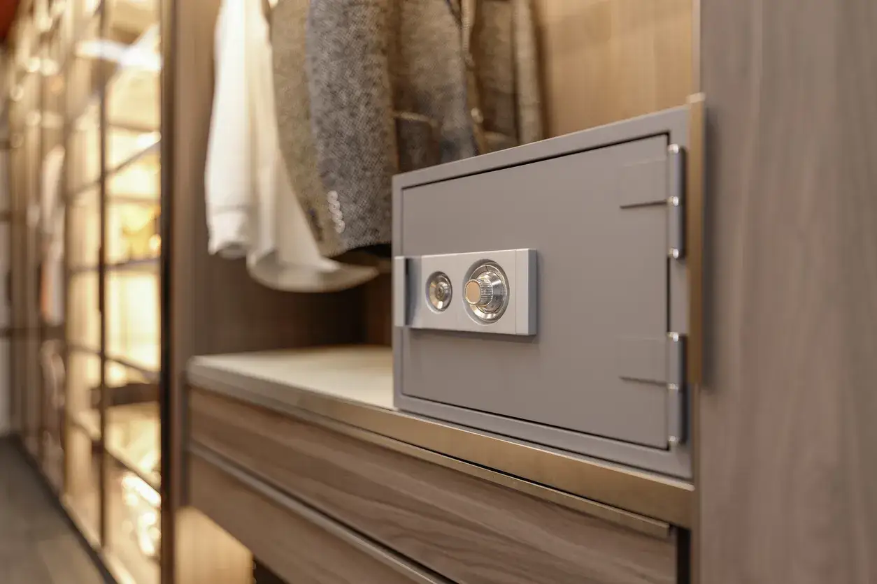 Caja fuerte gris con dial de combinaci&oacute;n, oculta entre ropa y estantes de un armario moderno.