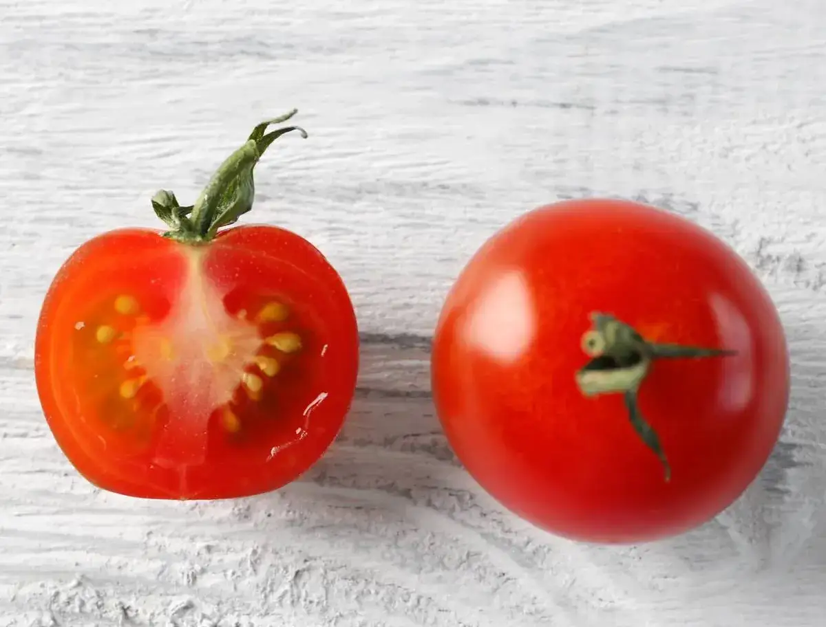 Une tomate entière et une coupée en deux, révélant ses graines. L'idée de faire ses graines de tomates est simple avec ces fruits mûrs.