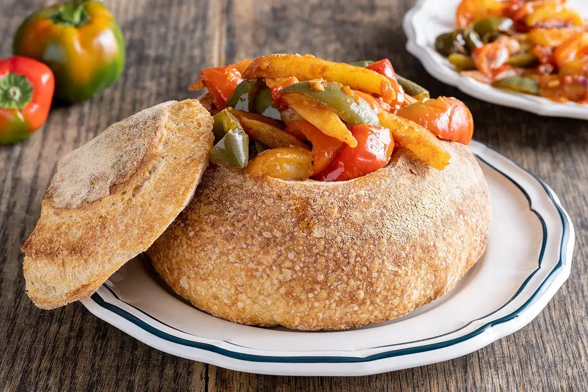 Pipi e patate in un pane scavato, un piatto rustico e colorato.
