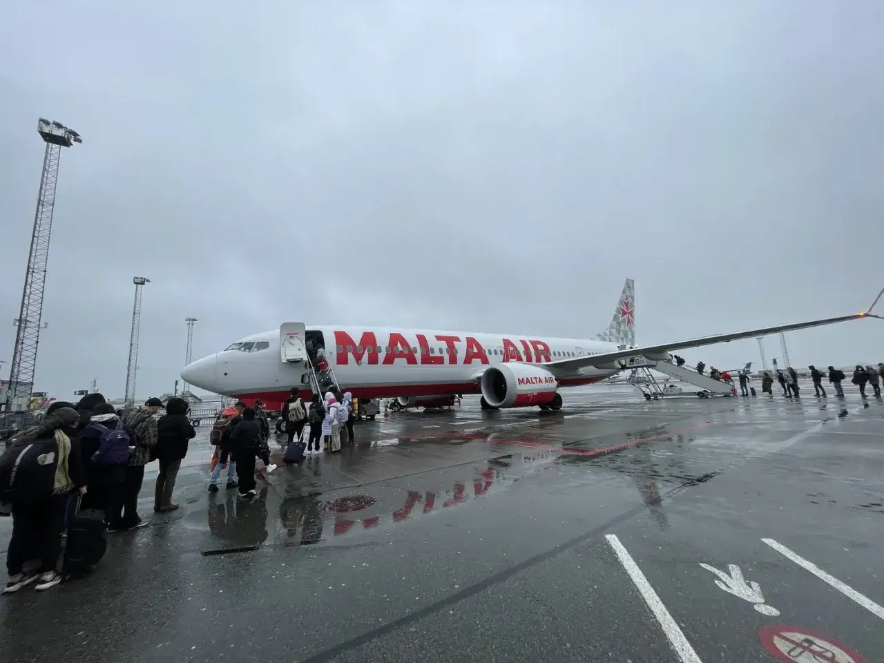 Passagerare går ombord på ett Malta Air-plan på en regnig dag.