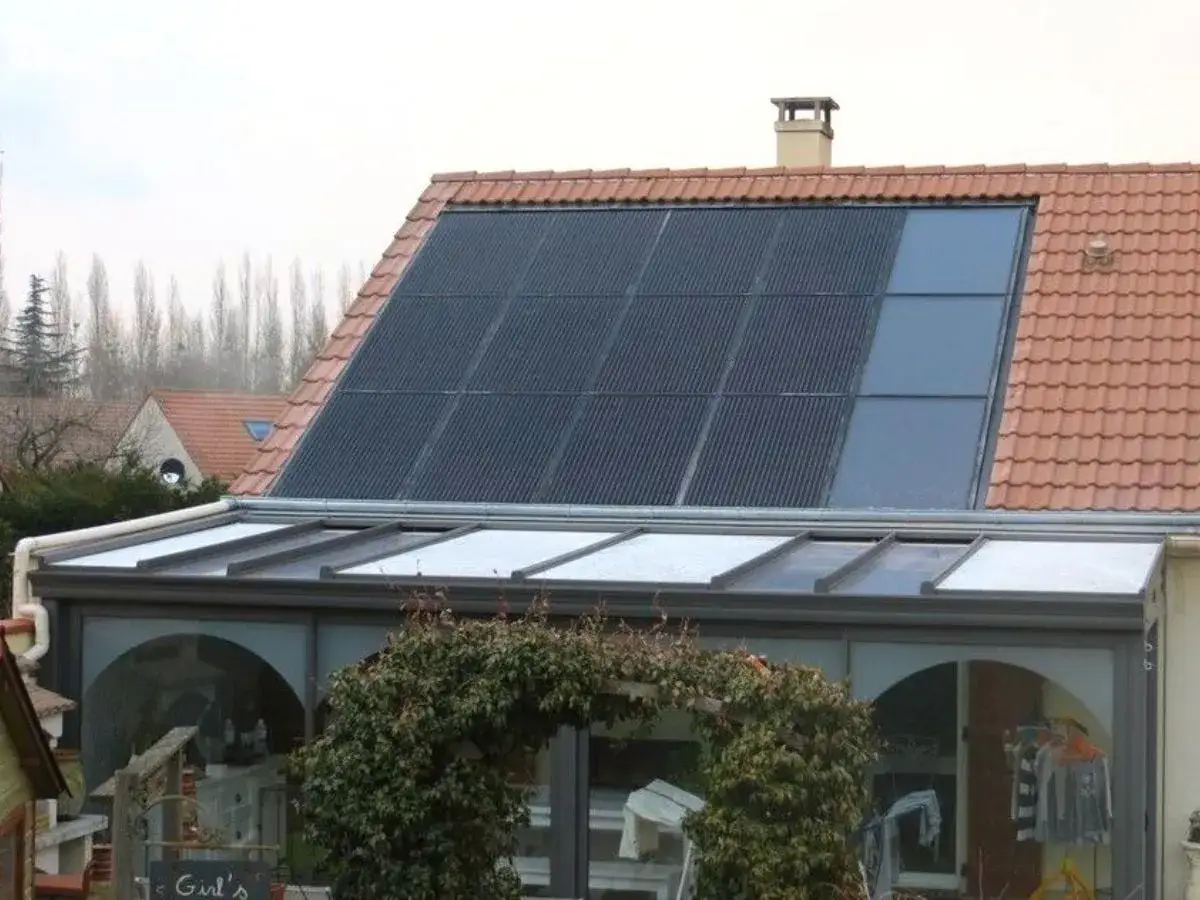 Panneaux solaires a&eacute;rovolta&iuml;ques int&eacute;gr&eacute;s sur un toit de tuiles rouges, au-dessus d'une v&eacute;randa vitr&eacute;e.