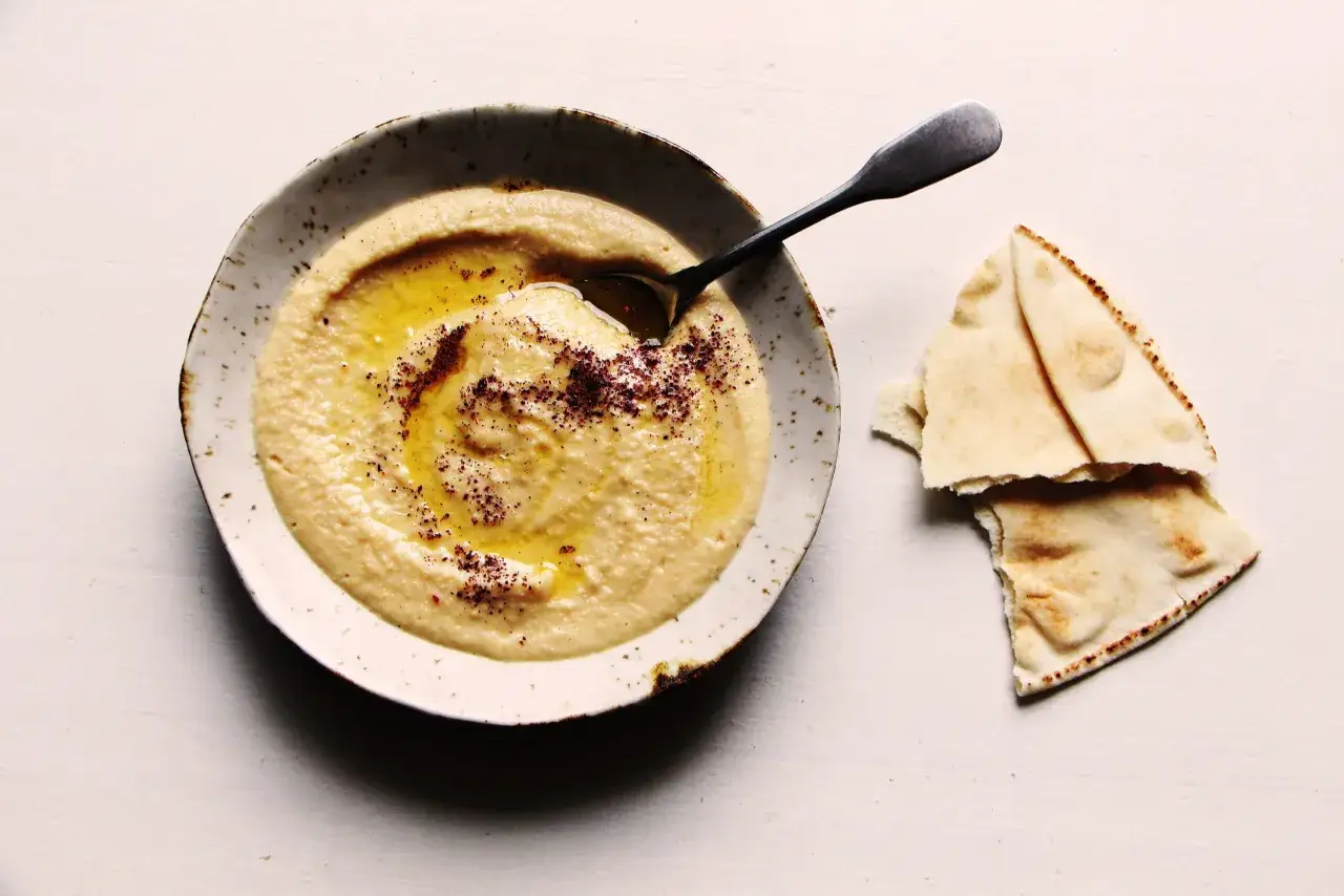Houmous cr&eacute;meux dans un bol, arros&eacute; d'huile d'olive et saupoudr&eacute; d'&eacute;pices. Une recette simple &agrave; d&eacute;guster avec du pain pita.