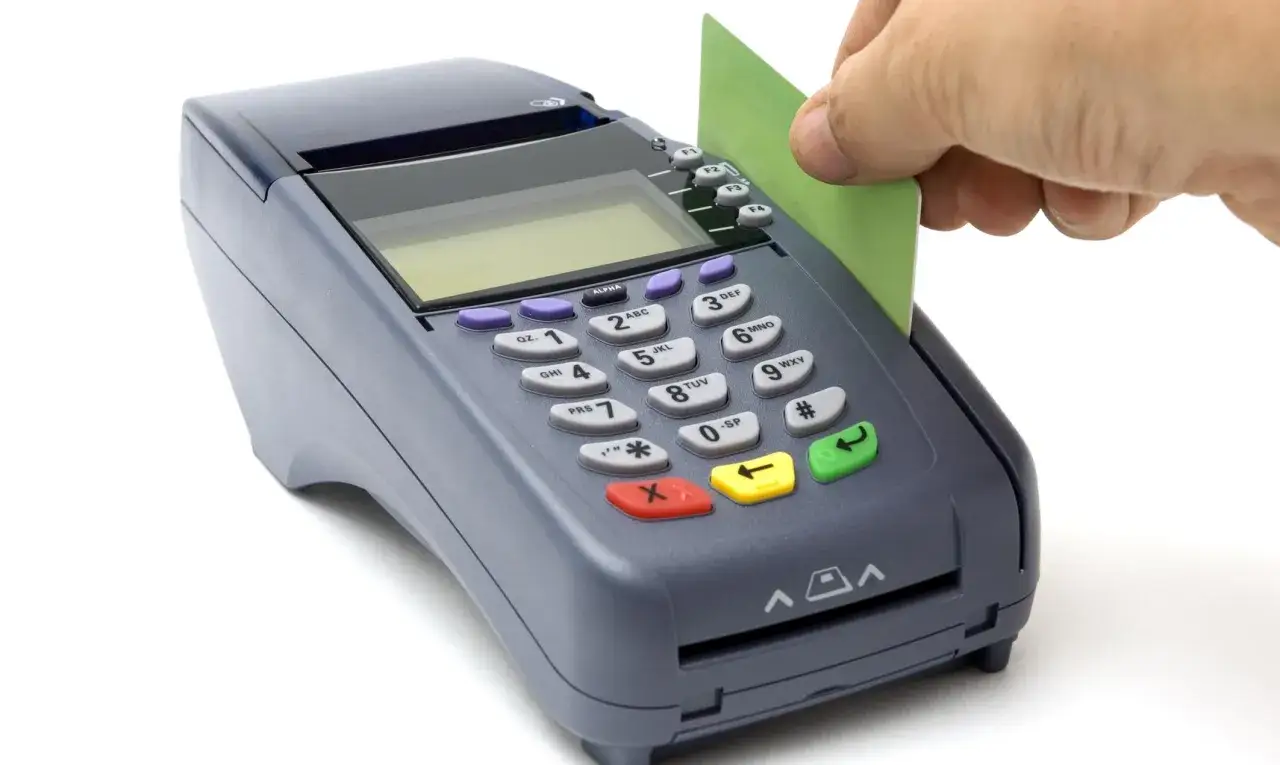 Ręka wkłada zieloną kartę do terminala PKO. Może to być początek transakcji lub próba zrealizowania chargeback PKO.