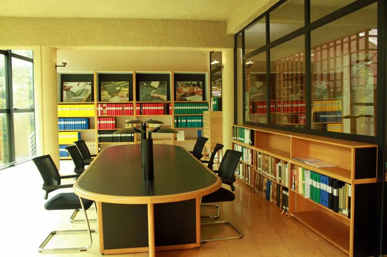 Salle de r&eacute;union lumineuse avec une grande table ovale, des chaises noires et des &eacute;tag&egrave;res remplies de dossiers color&eacute;s. Un espace id&eacute;al pour la recherche, comme dans une publicit&eacute; ad 79.
