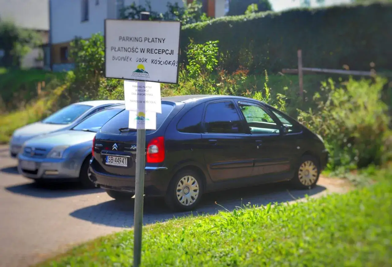 Parking płatny w Jaworzynce, blisko trójstyku. Samochody stoją przy drodze, obok znaku informującego o płatności w recepcji.