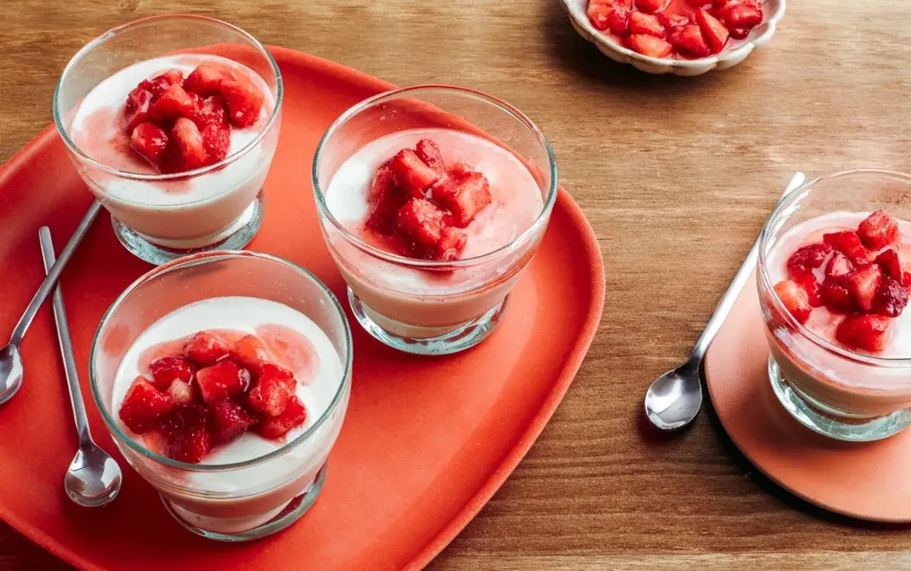 Quatre panna cotta fraise cr&eacute;meuses dans des verres, garnies de fraises fra&icirc;ches coup&eacute;es. Un d&eacute;lice fruit&eacute; !