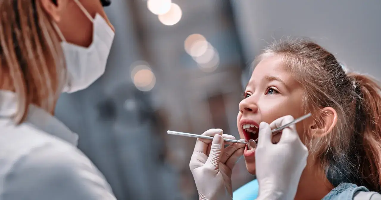 Mała dziewczynka u dentysty, który bada jej zęby. To normalny etap rozwoju, gdy u 5 latka następuje wypadanie zębów mlecznych.